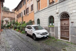 A white car parked on a cobblestone street in a historic area with buildings featuring arched windows and a wooden door. - One Bedroom Apartment (Roma)