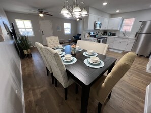A modern kitchen with white cabinets, stainless steel appliances, and a dining area with a dark wooden table and chairs.