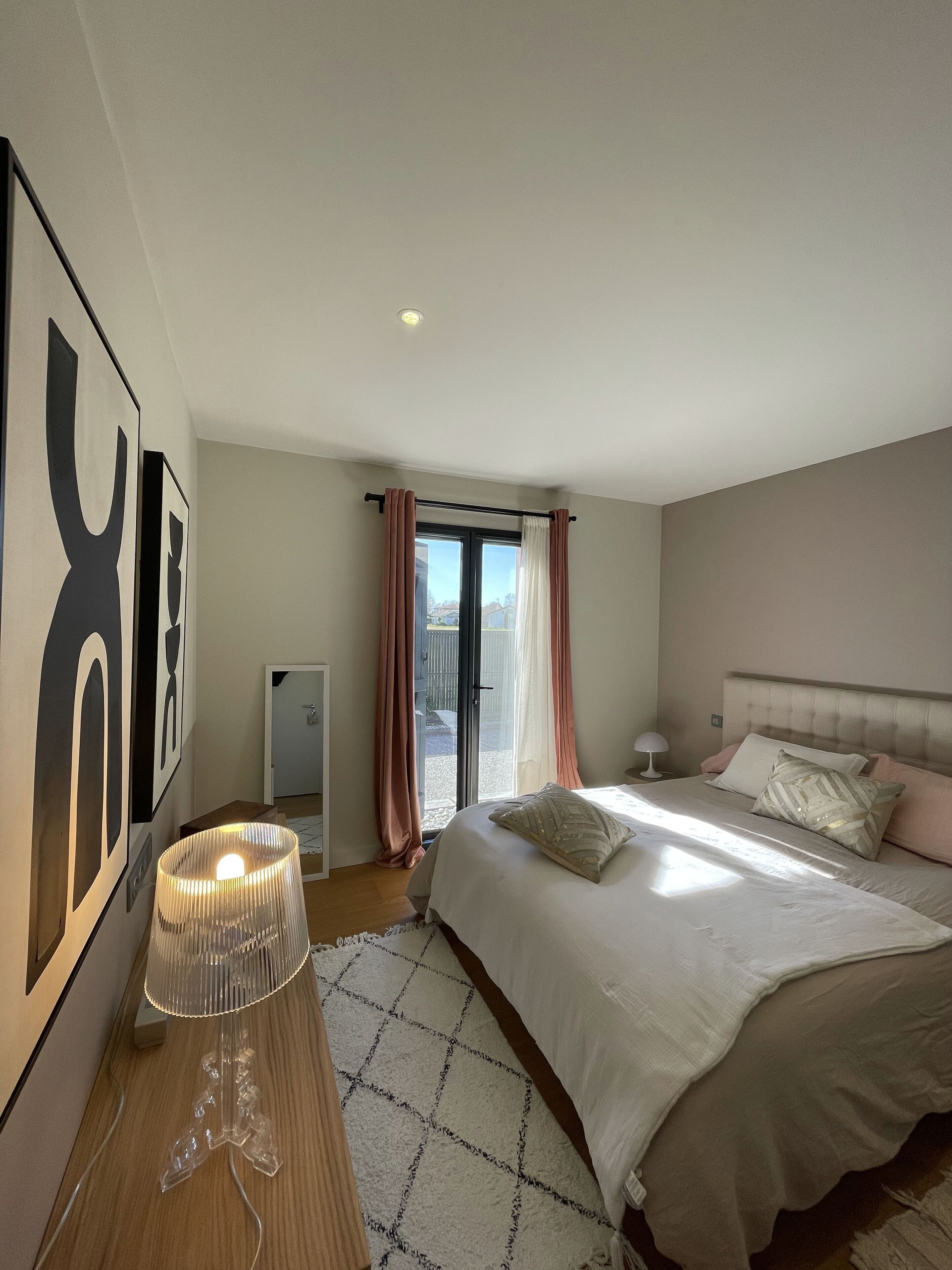 A bedroom with a bed, a bedside table with a lamp, a wall-mounted TV, and a sliding glass door leading to an outdoor area.