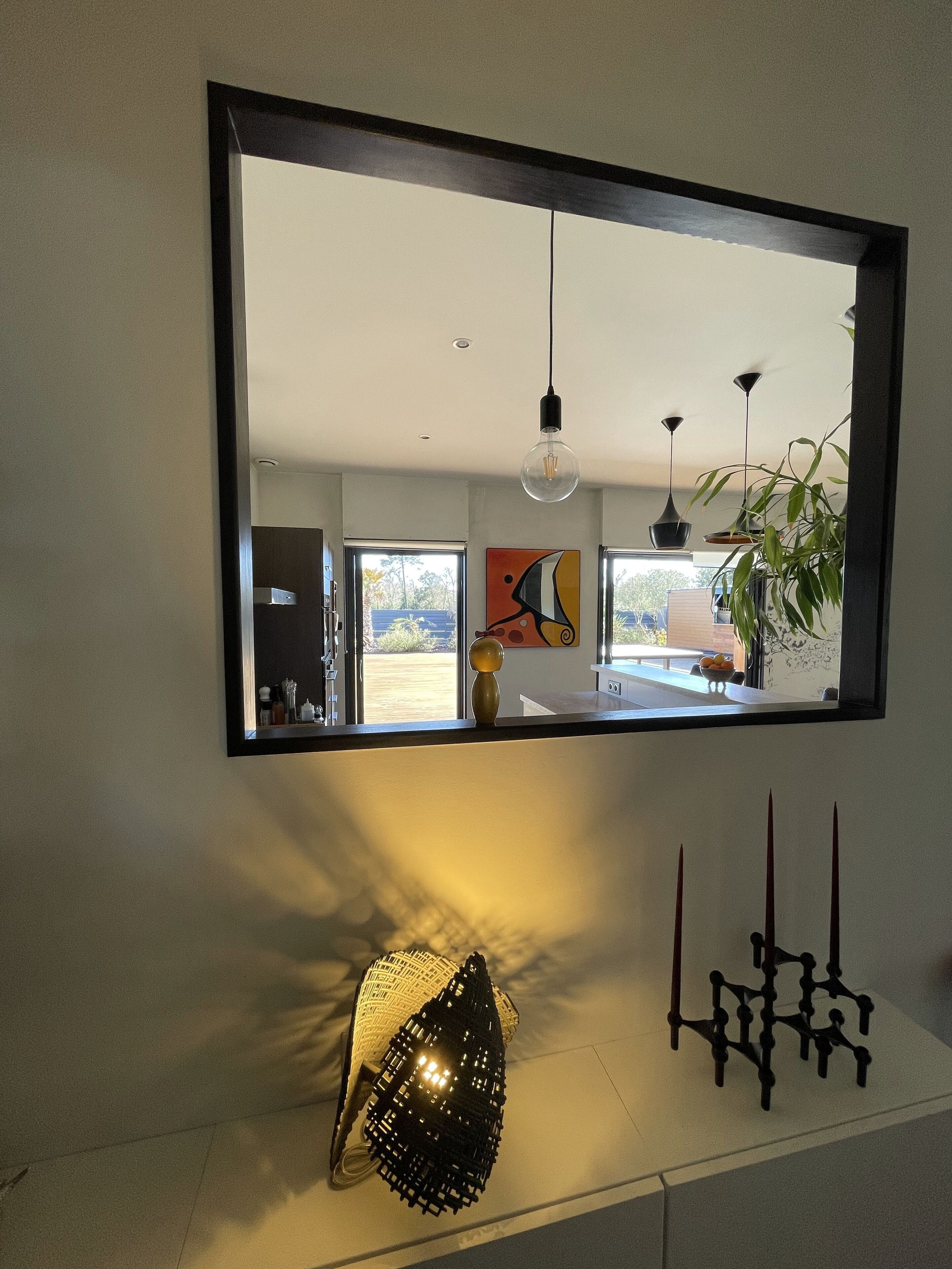 A modern interior with a large mirror, pendant lights, and decorative items on a white surface.