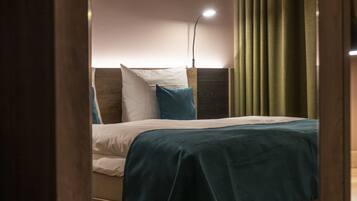 Una cama bien tendida con una colcha color turquesa y almohadas blancas, un cabecero de madera y una lámpara de noche.