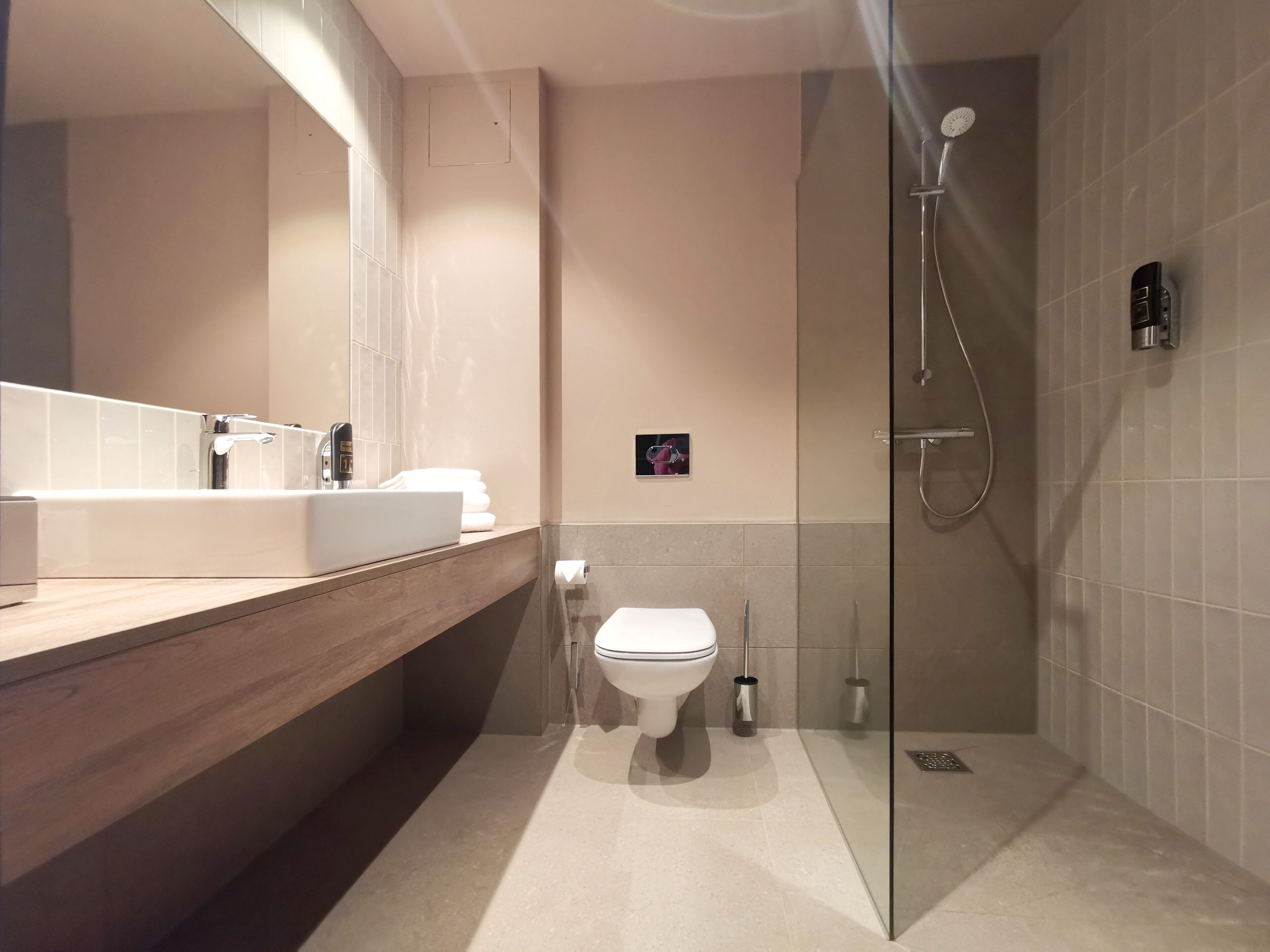 Un baño moderno con ducha acristalada, tocador de madera con lavamanos blanco y un inodoro.