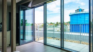 Un interior moderno con un puerta de cristal corredera que da a un balcón con vistas a un tanque de agua azul y edificios residenciales.