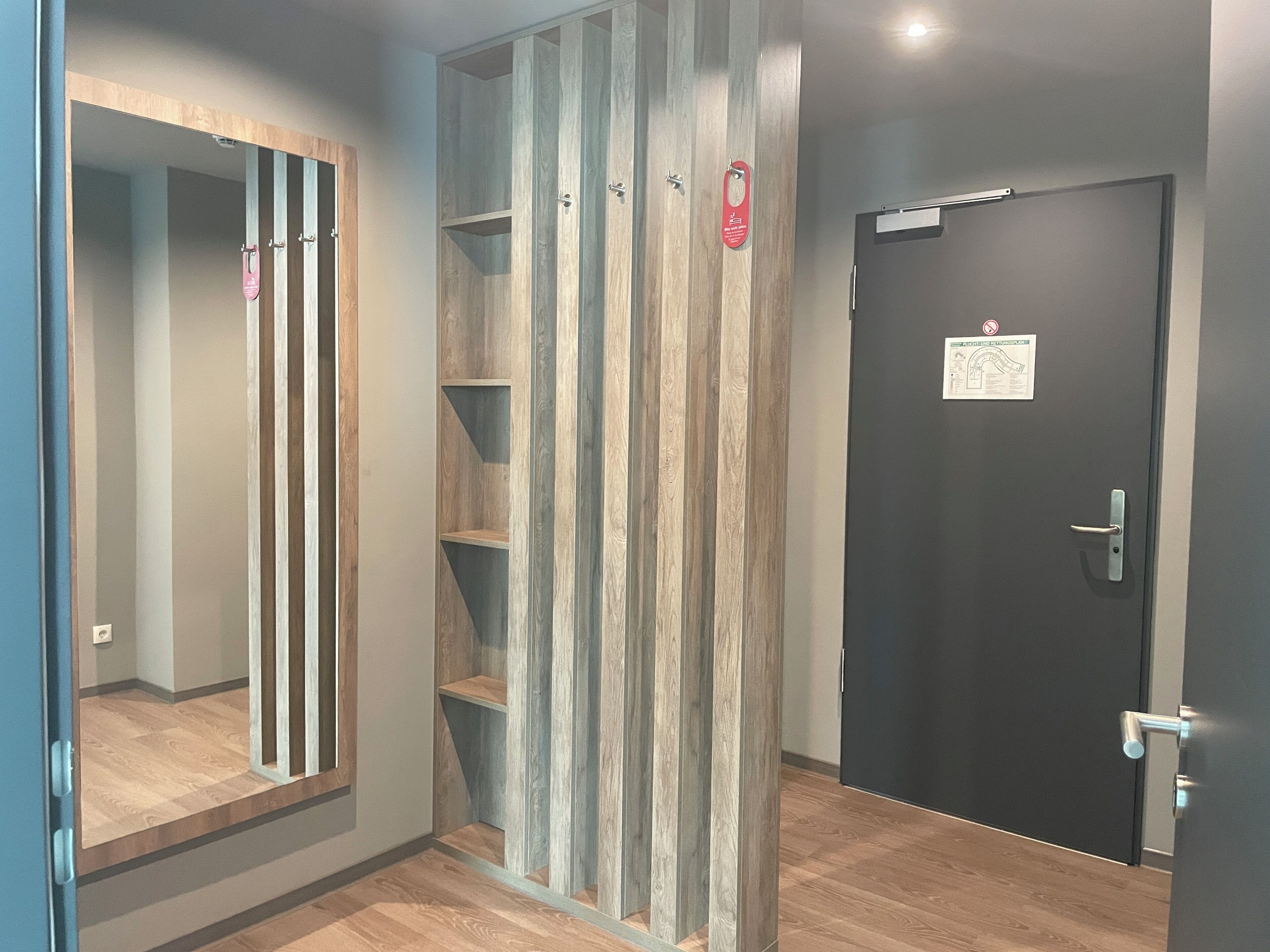 A hallway with a wooden panel wall, a black door with a sign, and a mirror on the left.
