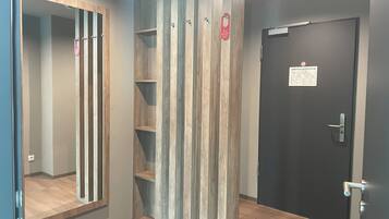 A hallway with a wooden panel wall, a black door with a sign, and a mirror on the left.