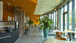 Un restaurante moderno con una barra larga, varias mesas y sillas. Amplias ventanas que permiten luz natural y vistas a la calle.