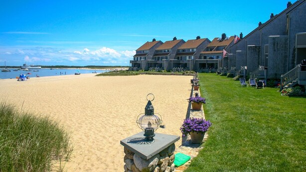 Um hotel à beira-mar com uma fileira de quartos, uma praia de areia e um céu claro.