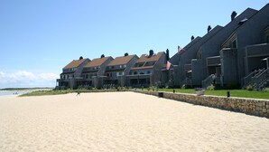 Um hotel à beira-mar com edifícios de vários andares, uma praia arenosa em primeiro plano e um céu azul e límpido.