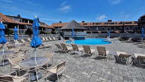 Uma área à beira da piscina com espreguiçadeiras, guarda-sóis e uma piscina pequena.