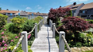 Uma ponte de madeira que leva a uma área residencial com casas e jardins exuberantes.