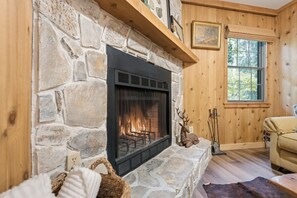 A stone fireplace with a fire, a wooden ceiling, a window, and a couch. - Walk to town,covered deck dining,wood-burning fireplace (Highlands)