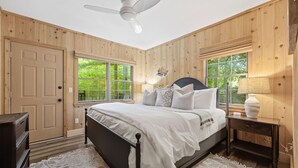 Une chambre à coucher comprenant un lit, une table de chevet, une lampe, une commode et un ventilateur de plafond.