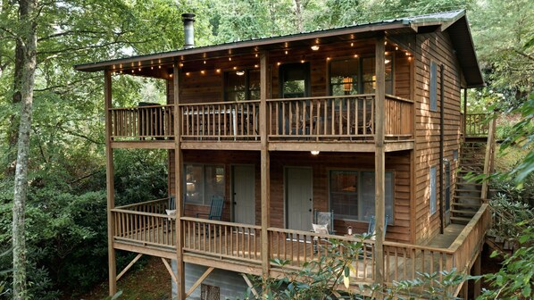 Een houten chalet met twee verdiepingen en een balkon, omringd door bomen.