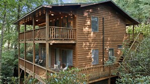 Une cabane en bois à deux étages, dotée d’un balcon et entourée d’arbres.
