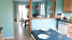 Un comedor con una mesa preparada para dos, una zona de cocina con lavavajillas y un espejo que refleja la habitación.