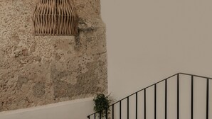 Una escalera con barandal negro, una planta en maceta y un muro con textura.