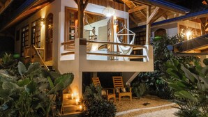 A two-story wooden house with a balcony, surrounded by tropical plants and a gravel pathway. - Bungalow Pacifico - Beach Chic! (North Santa Teresa)