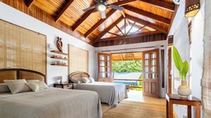 A bedroom with two beds, wooden ceiling beams, a ceiling fan, and a view of the outdoors. - Bungalow Pacifico - Beach Chic! (North Santa Teresa)