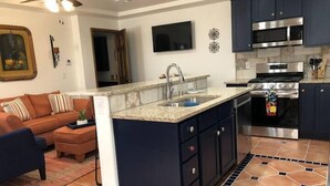 A modern kitchen with dark cabinets, a granite countertop, stainless steel appliances, and a large island with a sink. - Lovely 1-Bedroom Adobe Escape (Mesilla)