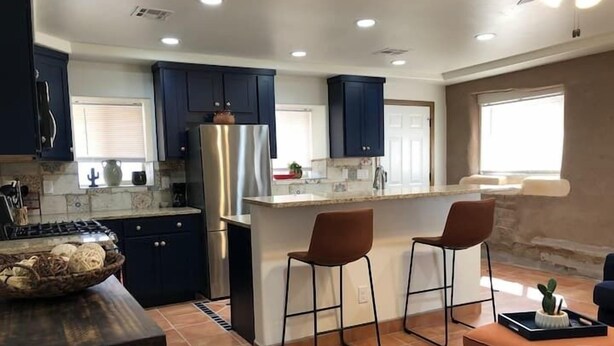 A modern kitchen with dark cabinets, stainless steel appliances, and a central island with bar stools. - Lovely 1-Bedroom Adobe Escape (Mesilla)