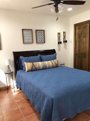 A bedroom with a large bed, a ceiling fan, and a wooden door.