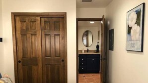 A bedroom with a large wooden door, a blue bedspread, a dark dresser, a mirror, and a framed picture on the wall. - Lovely 1-Bedroom Adobe Escape (Mesilla)