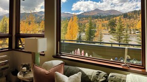 A room with a large window offering a view of autumn foliage and mountains.
