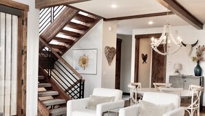 A spacious living room with a staircase, white furniture, and a chandelier.