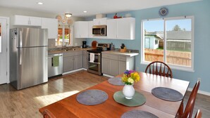 A modern kitchen with stainless steel appliances, a dining table with placemats, and a view of the backyard through a large window. - Atargatis "the first mermaid"; an updated & spacious home, close to everything! (Brookings)