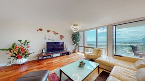 Relax in this stylish living room with a large flat-screen TV, comfortable sofa, and armchair, offering a view of the coastal cityscape.