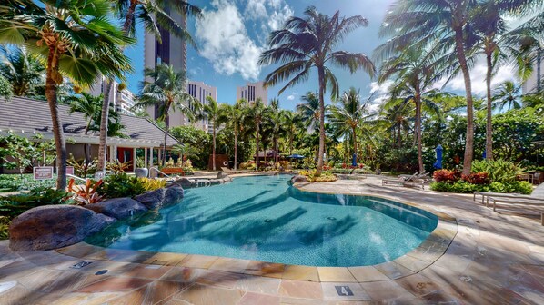 A pool area with palm trees, lounge chairs, and a building in the background.