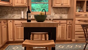 Una cocina con armarios de madera, una ventana que ofrece vistas a zonas verdes, una mesa de madera con un cuenco de plátanos y una botella de vino.