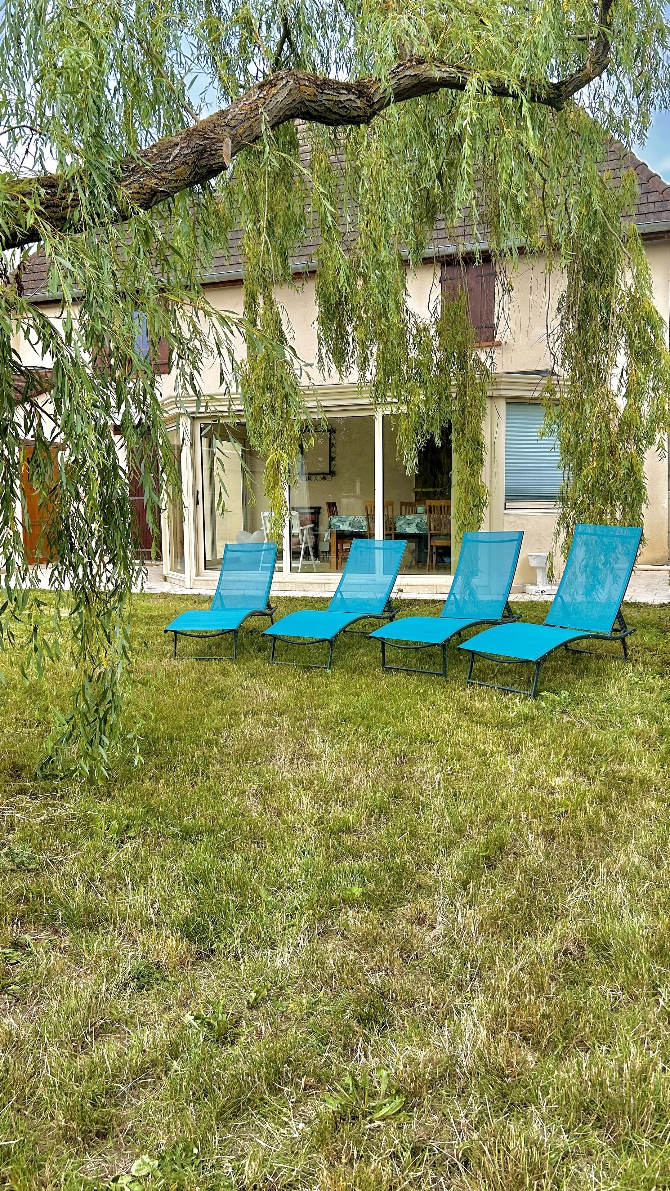 A house with a covered patio area, a lawn, and four blue lounge chairs.