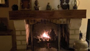 A fireplace with a mantel decorated with various items, a wall-mounted mirror above it, and a tiled floor. - The Nebula (notre dame de l'isle)