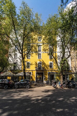 Un edificio amarillo con varias ventanas y una puerta, rodeado de árboles.