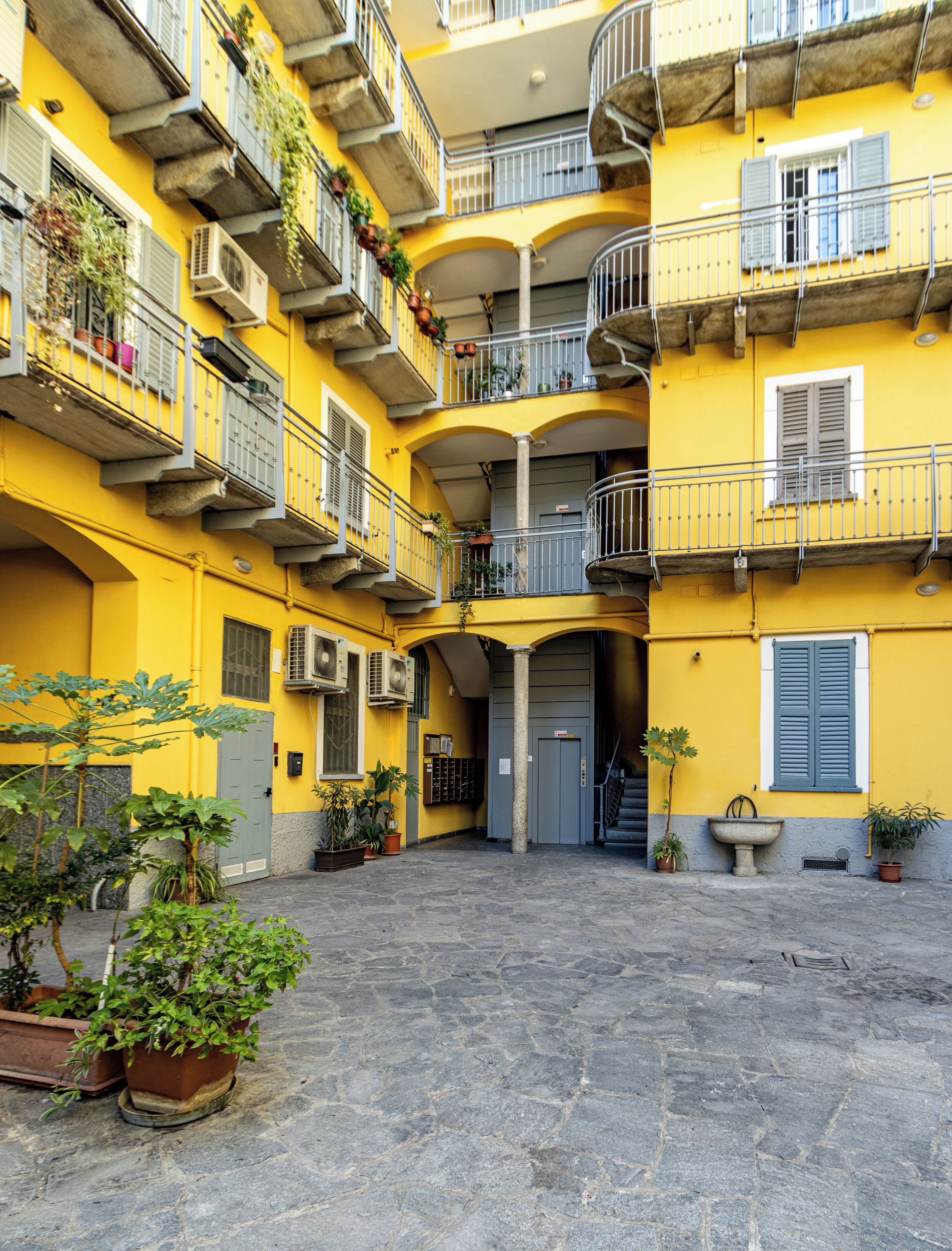 Un cortile con un edificio giallo, diversi balconi e piante in vaso.