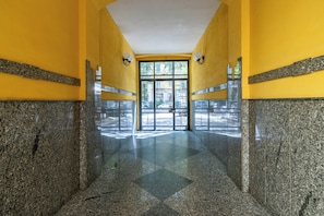 Un pasillo con piso de granito pulido, paredes amarillas y una puerta de vidrio que da al exterior.