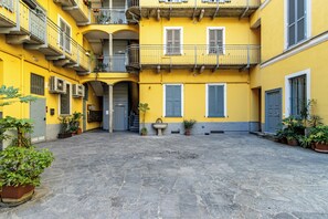 Un patio con un edificio amarillo, suelo de piedra y plantas en macetas.