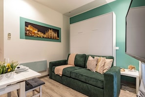 Ein modernes Wohnzimmer mit einem grünen Sofa, einem Flachbildfernseher, einem Tisch mit Blumen und einem gerahmten Bild an der Wand.