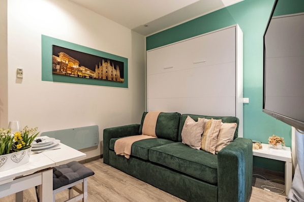 Una sala de estar moderna con un sofá verde, un televisor de pantalla plana, una mesa con un jarrón de flores y un cuadro en la pared.
