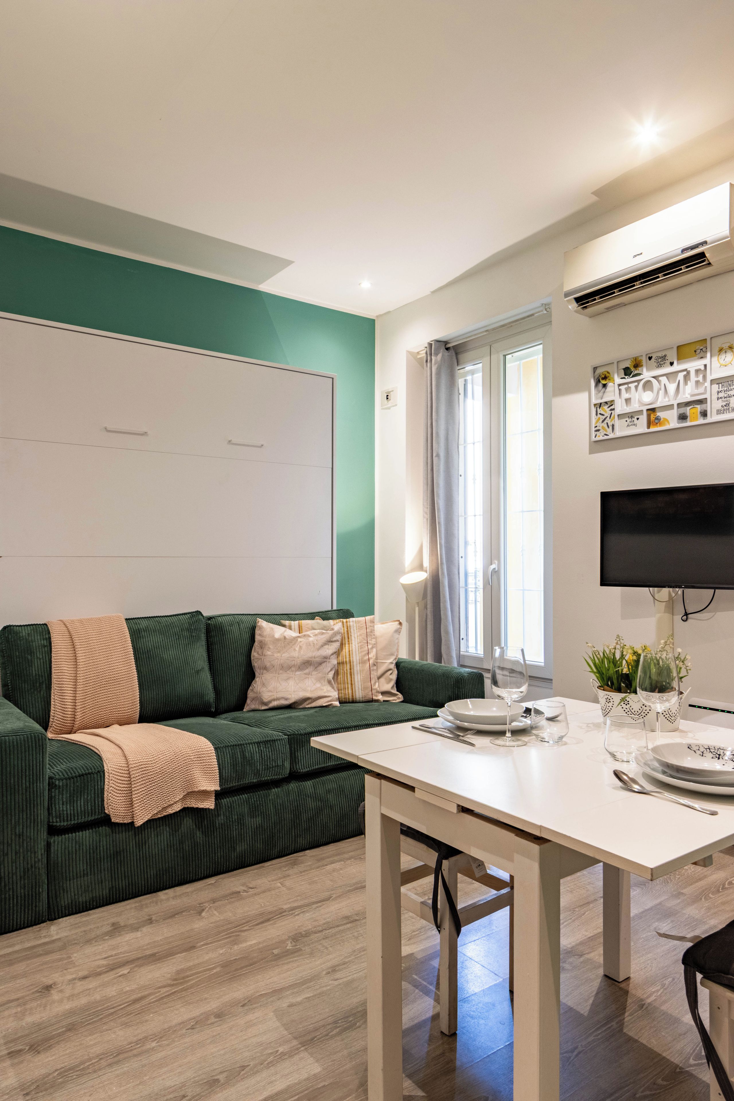 Ein modernes Wohnzimmer mit einem grünen Sofa, einem weißen Tisch und einem flachbildfernseher an der Wand.