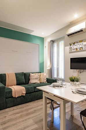 Una sala de estar moderna con un sofá verde, una mesa blanca y un televisor de pantalla plana montado en la pared.