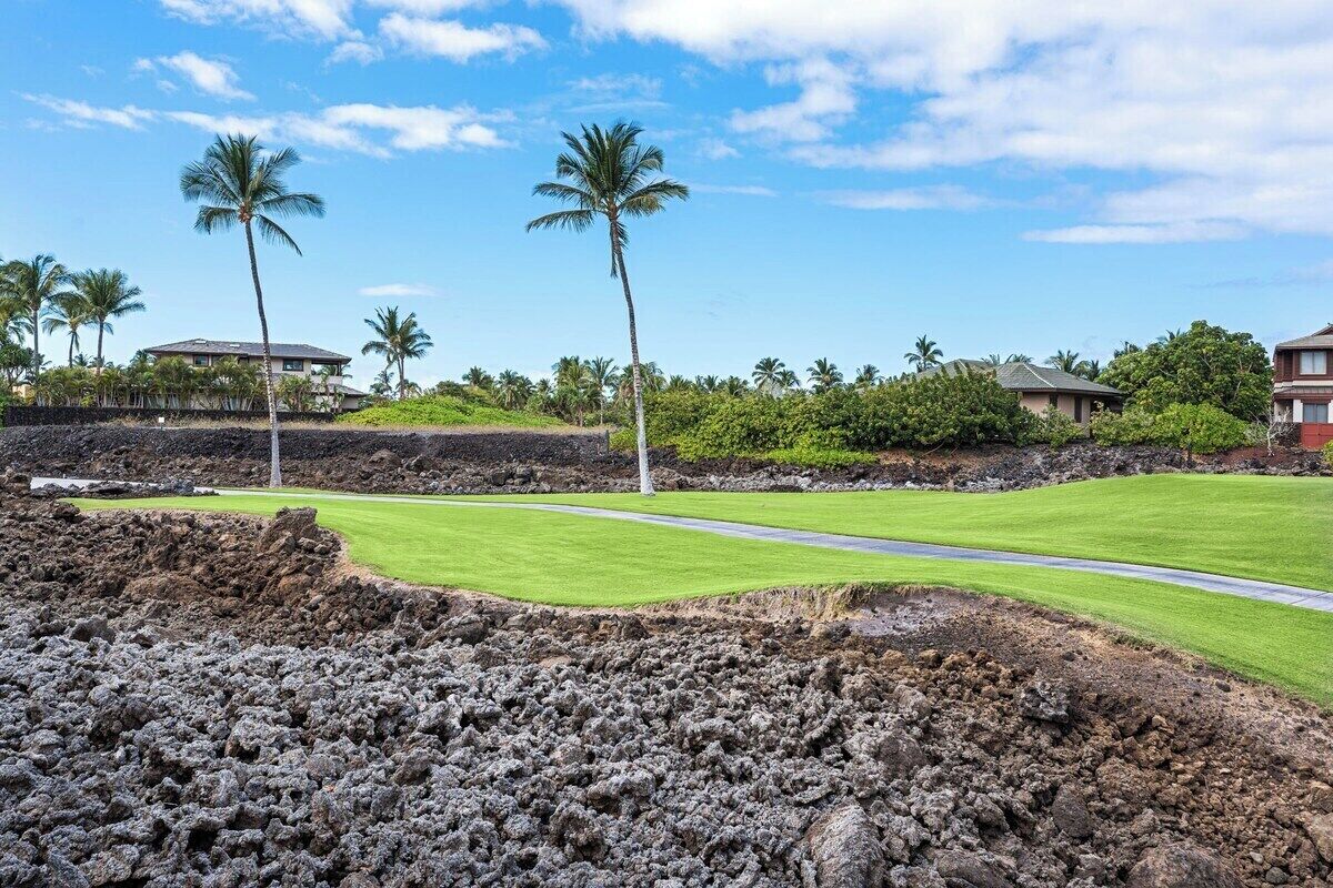 A golf course with a well-maintained green, a clear sky, and a few palm trees.