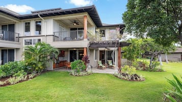 A two-story house with a covered patio, a lawn, and various plants.