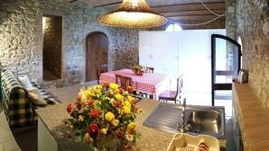 Ein rustikaler Raum mit Steinsandsteinwänden, einer Essecke mit rot-weiß kariertem Tisch, einer großen Blumenvase und einem Steinkreuz.