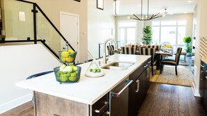 A modern kitchen with a central island, stainless steel appliances, and a dining area with a table and chairs. - STUNNING LUXURY BEACH HOUSE (Cleveland)