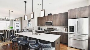 A modern kitchen with a central island, dark cabinetry, stainless steel appliances, and pendant lighting. - STUNNING LUXURY BEACH HOUSE (Cleveland)