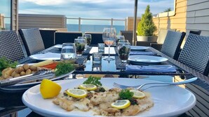 An outdoor dining area with a table set for two, featuring a seafood dish, a salad, and a lemon wedge. - STUNNING LUXURY BEACH HOUSE (Cleveland)