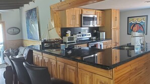 Una cucina con mobili in legno, un piano di lavoro nero e una grande isola. Sono presenti due sgabelli da bar e un modellino di una barca a vela.