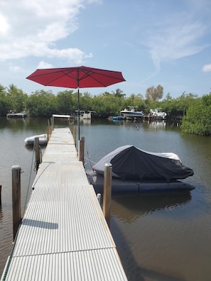Une jetée en bois s’avançant dans une étendue d’eau calme, avec un parasol rouge et des bateaux à l’abri.